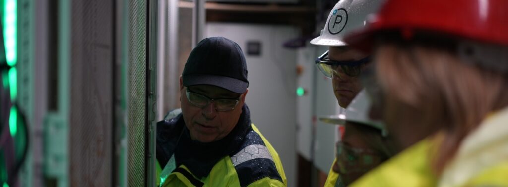 Technical services professionals in safety gear inspecting industrial equipment with green lighting in facility.